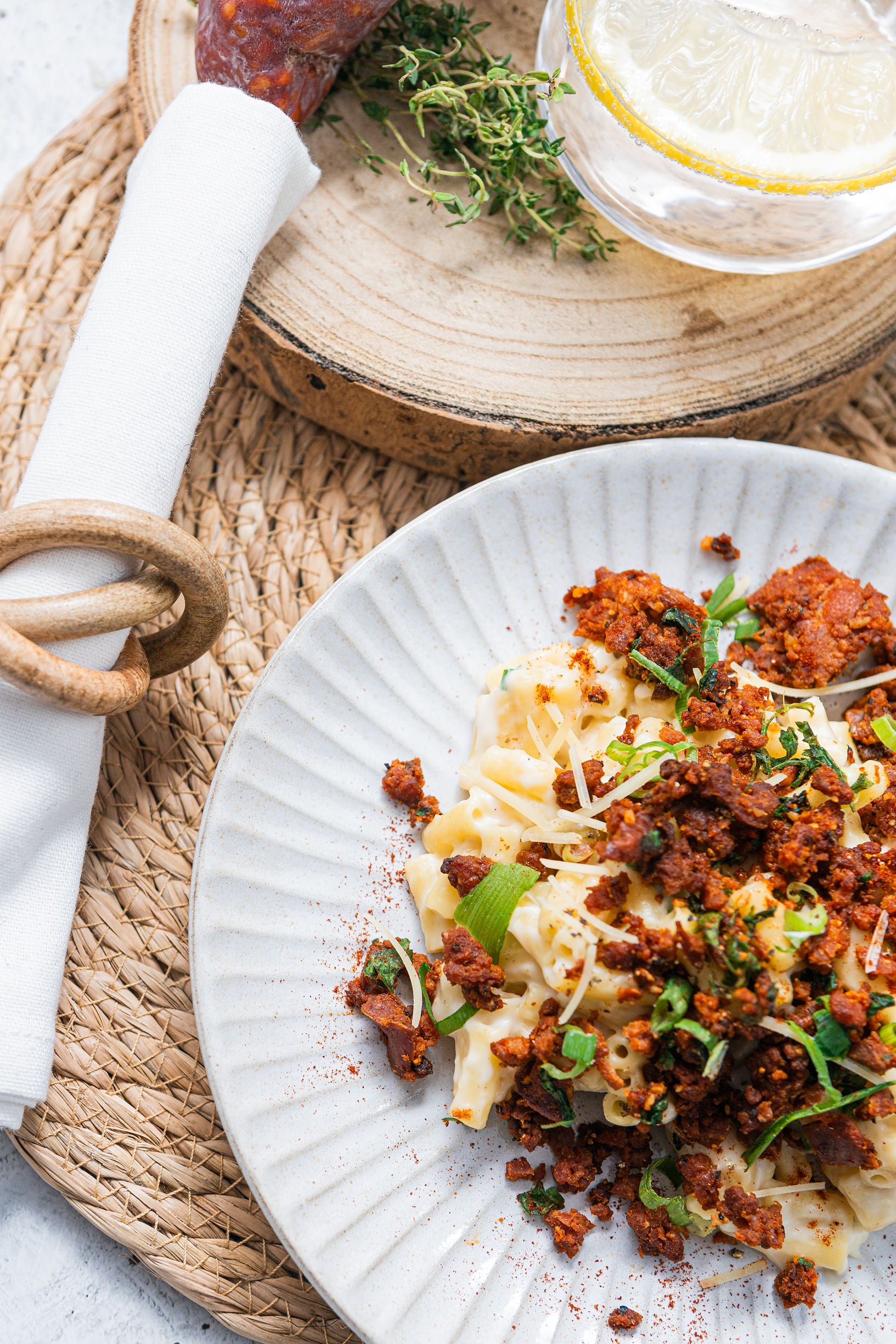Pasta dish with meat sauce on a white plate, placed on a woven mat.