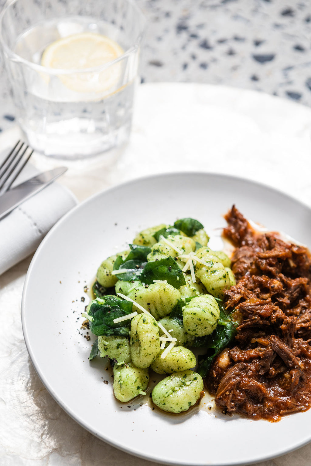 Plate of Brubecks gnocchi and brown meat on a white plate with a glass of water in the background.