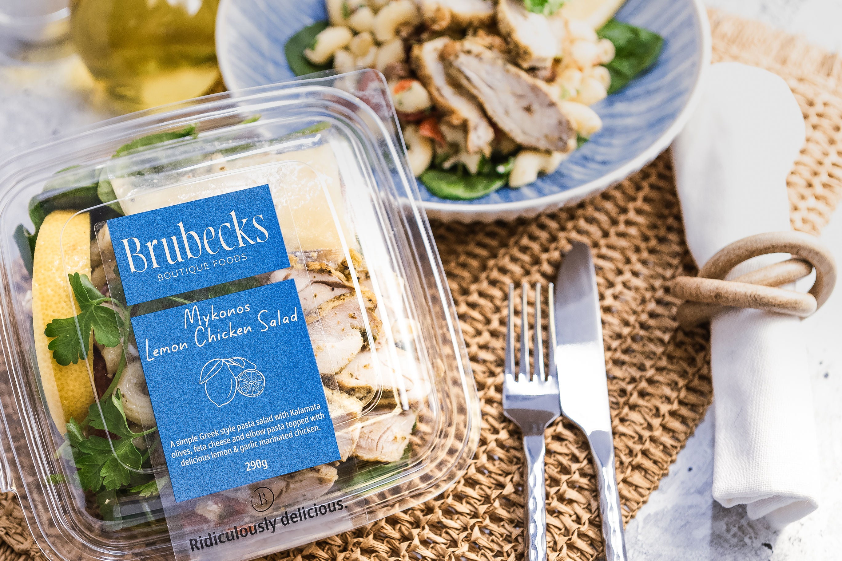 Brubecks Mykonos Lemon Chicken Salad packaging on a table with a salad and cutlery.