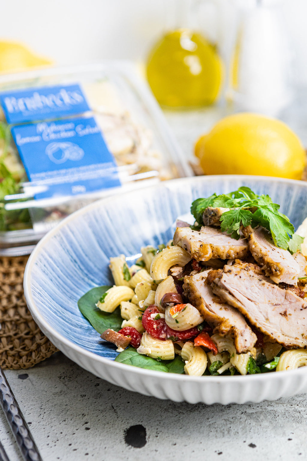 Pasta salad with meat and vegetables in a blue bowl on a light surface.