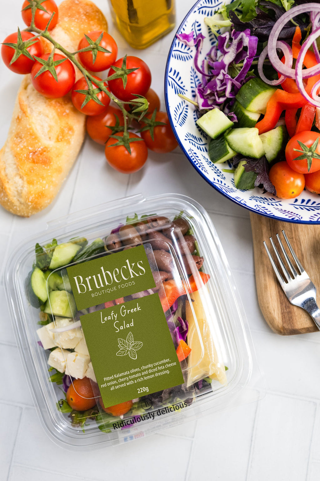 Brubecks salad packaging with a bowl of salad, tomatoes, and bread on a white surface