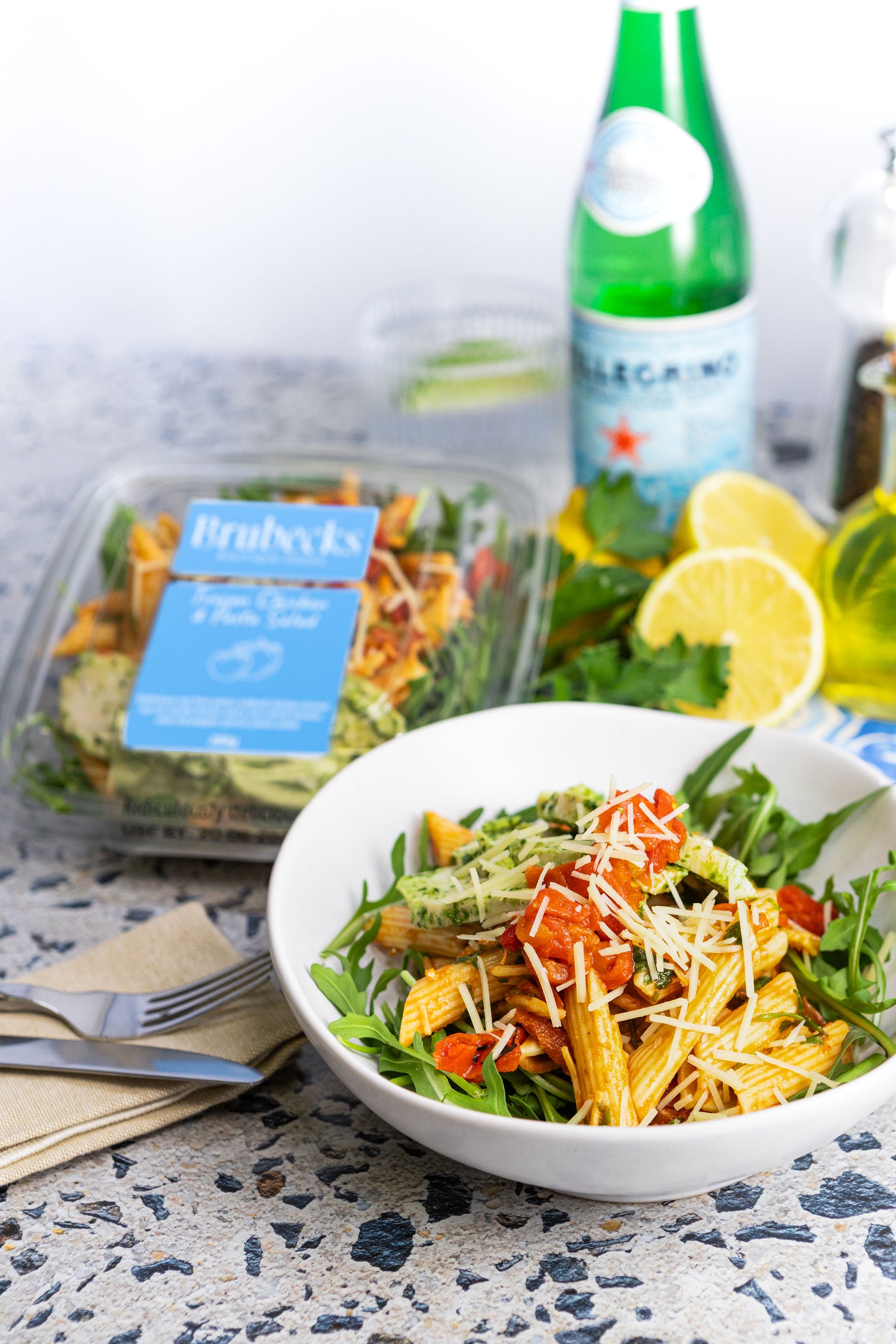 Salad in a bowl with a bottle of water and a salad container in the background.