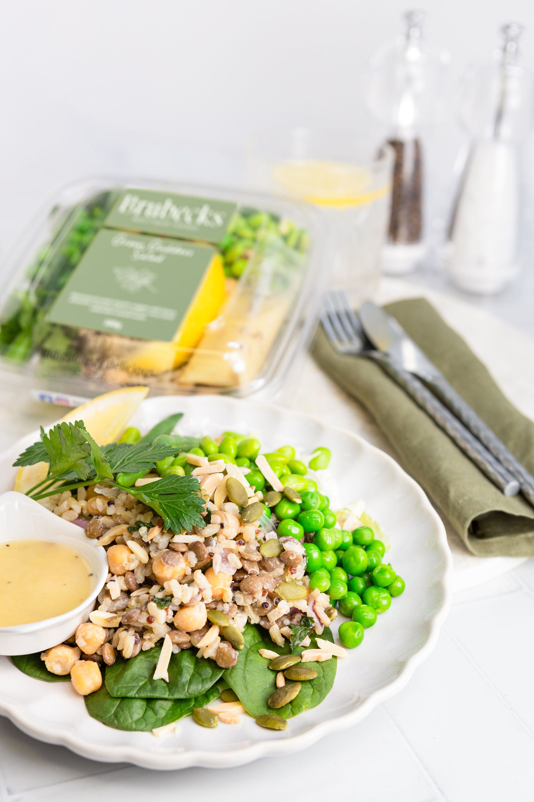 Plated salad with chickpeas, greens, and peas on a white plate with a container of dressing in the background.