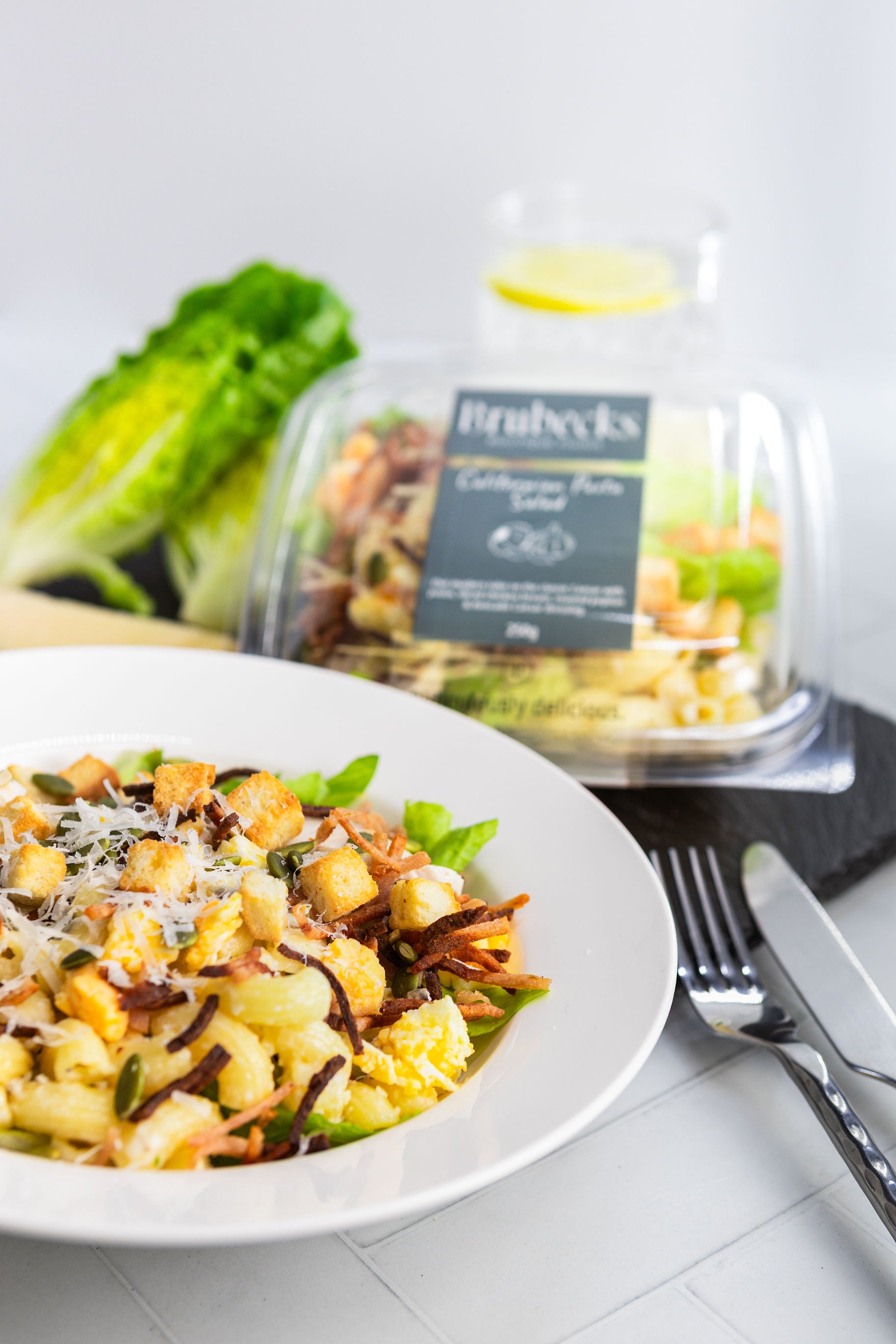 Pasta salad on a plate with a container of salad in the background