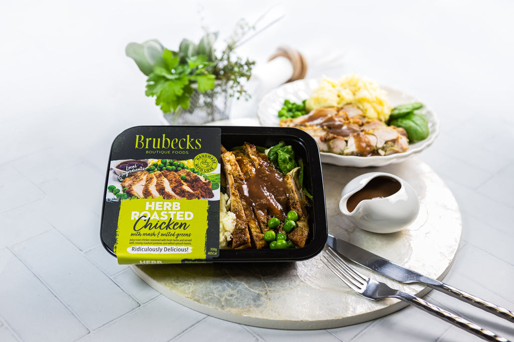 Brubecks herbed roasted chicken packaging on a table with a dish of chicken and vegetables.