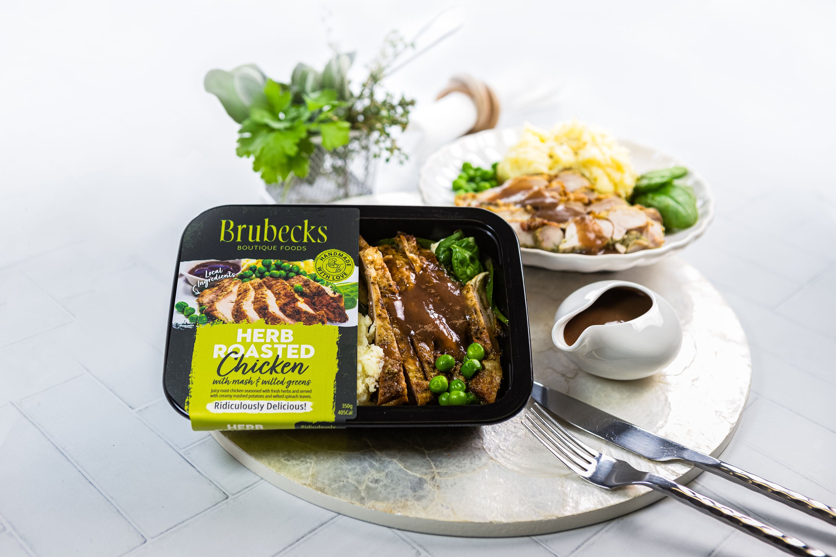 Brubecks herbed roasted chicken packaging on a table with a dish of chicken and vegetables.