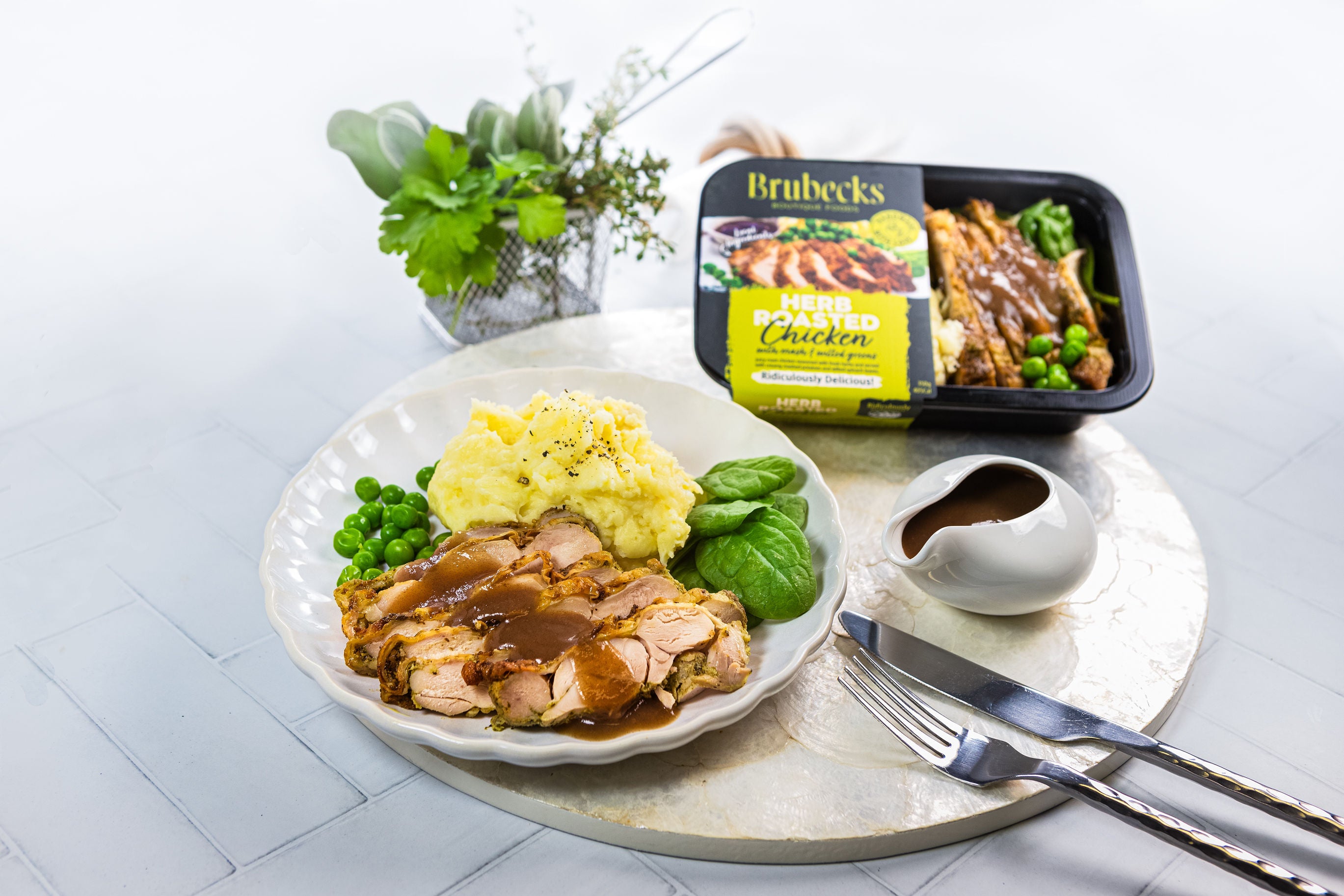 Plated roasted chicken with mashed potatoes and vegetables, accompanied by a Brubeck's branded packaging.