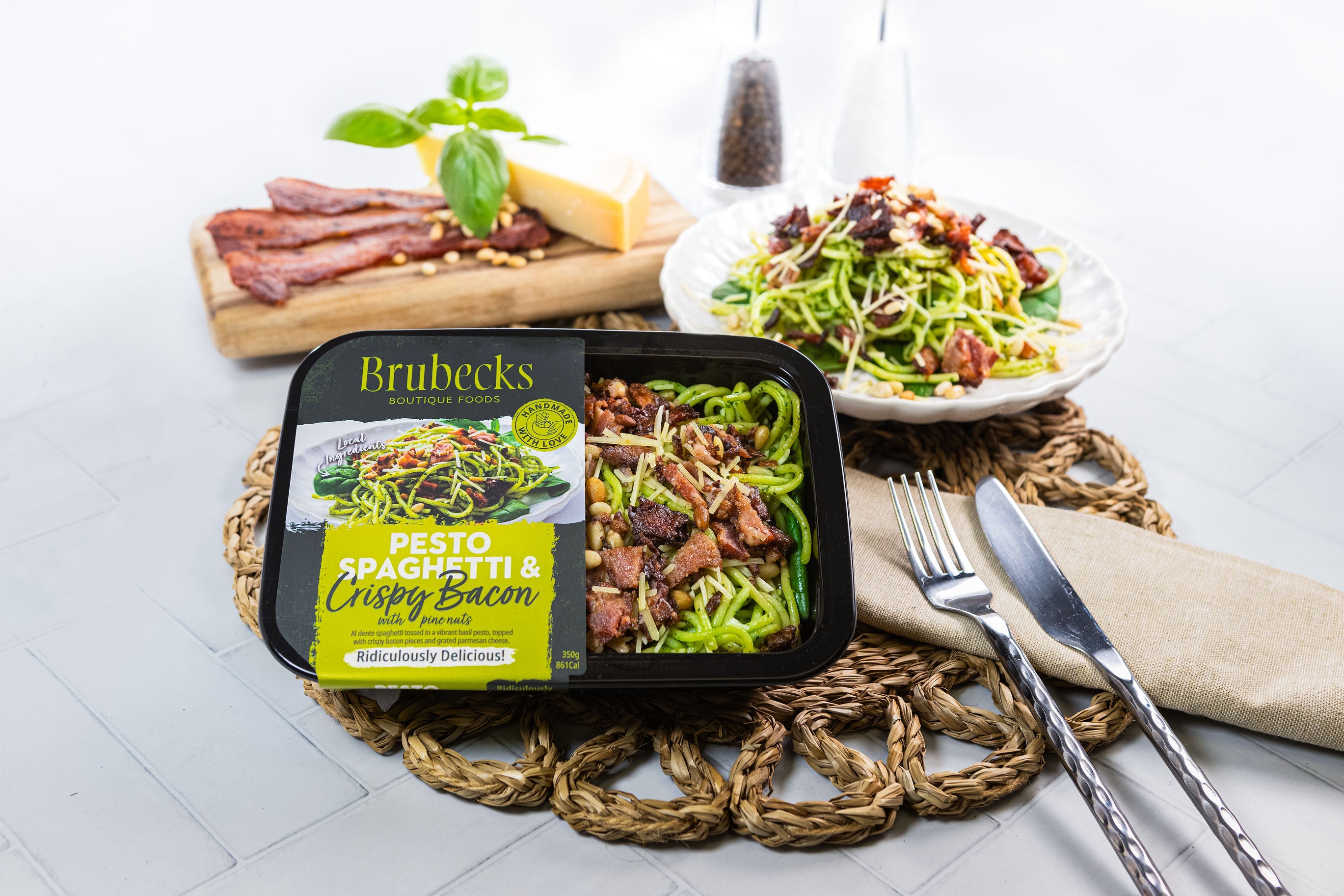 Brubecks pesto spaghetti with crispy bacon packaging on a table with a pasta dish and ingredients.