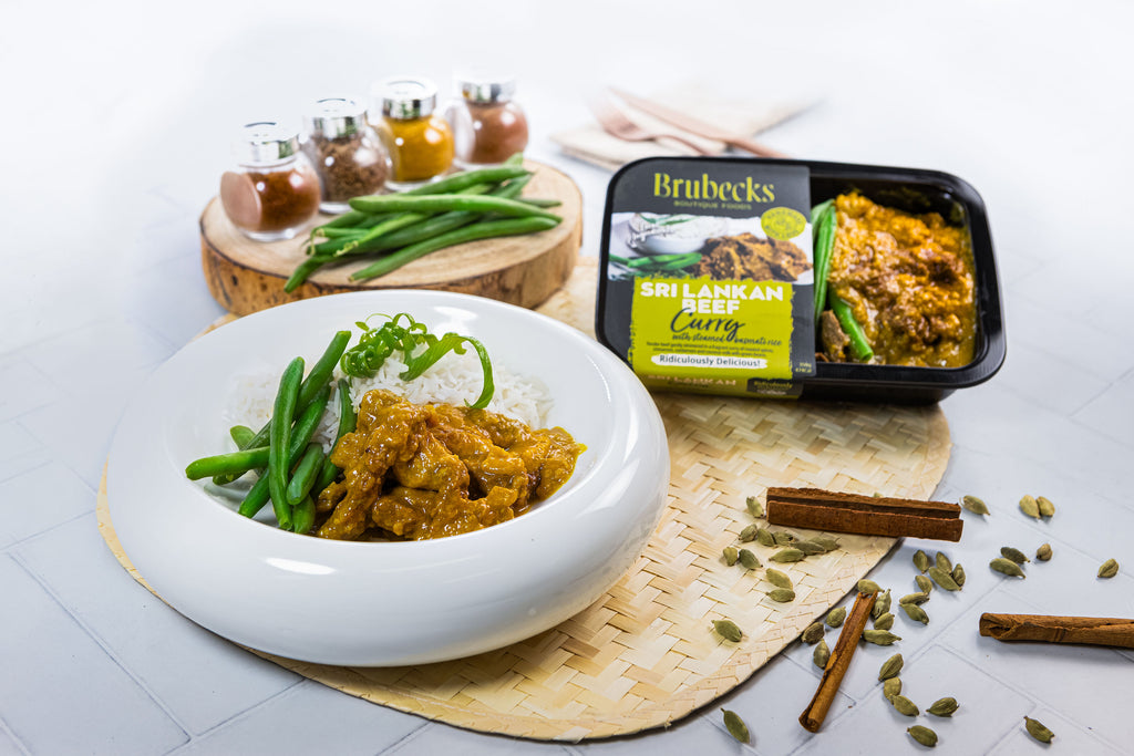Bowl of curry with rice and green beans, Brubecks Sri Lankan Curry package, and spices on a white surface.