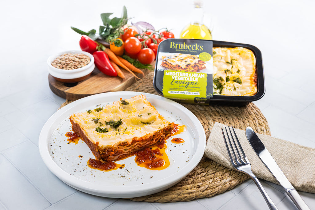 Lasagna on a plate with Brubeck's lasagne packaging and fresh vegetables in the background.