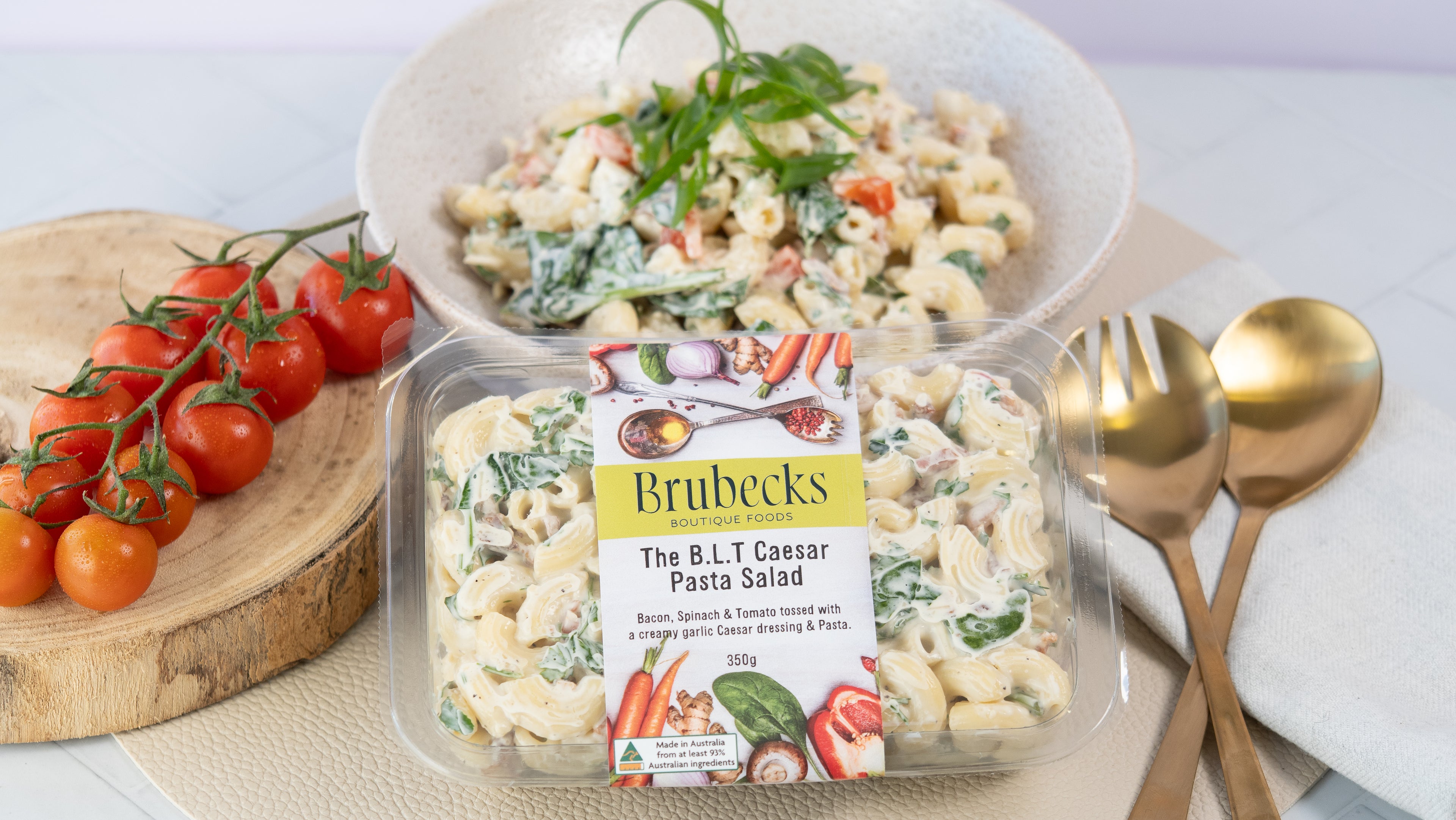 Brubecks B.L.T Caesar Pasta Salad packaging with a bowl of salad and cherry tomatoes on a table.
