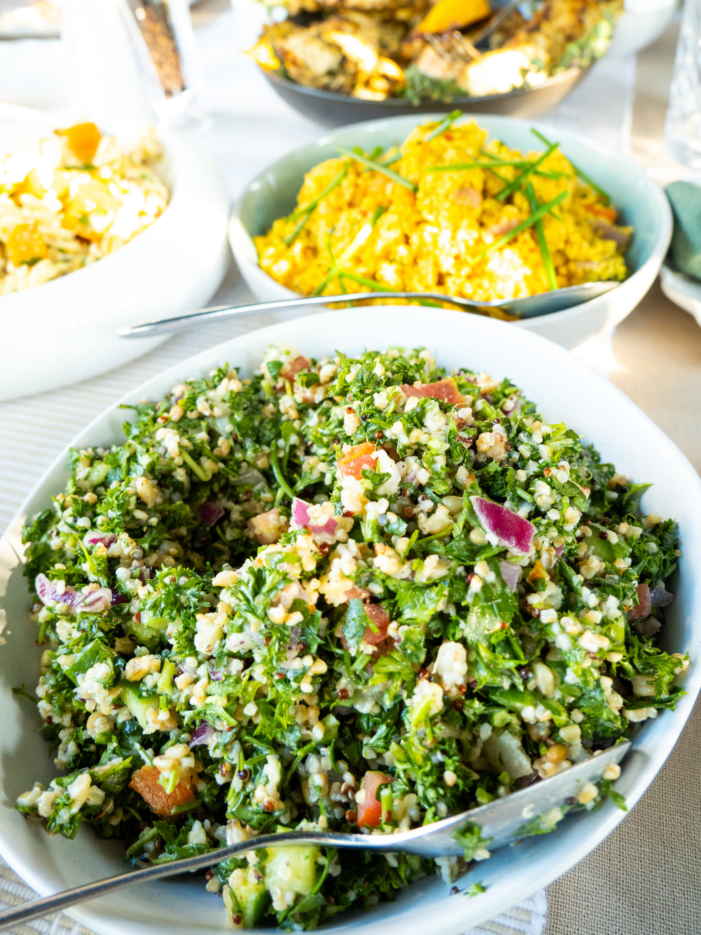 Bowl of green salad with a fork on a white plate, surrounded by other dishes.