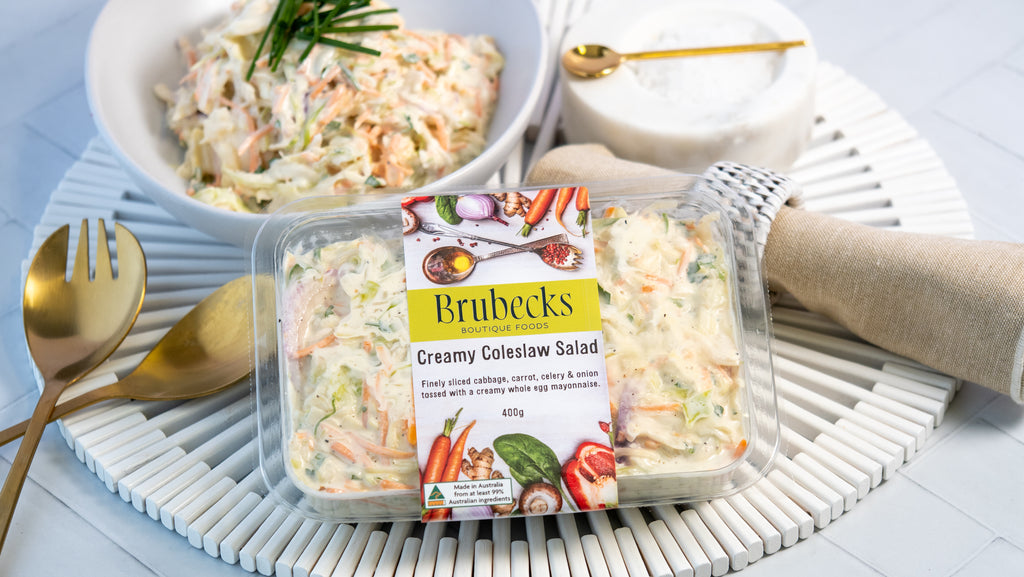 Brubecks Creamy Coleslaw Salad packaging with a bowl of salad and utensils on a table.