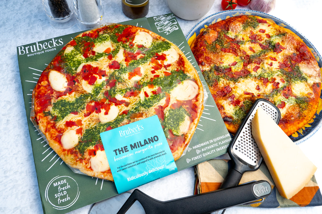 Two pizzas on trays with 'Brubeck's' branding, a grater, and a block of cheese.