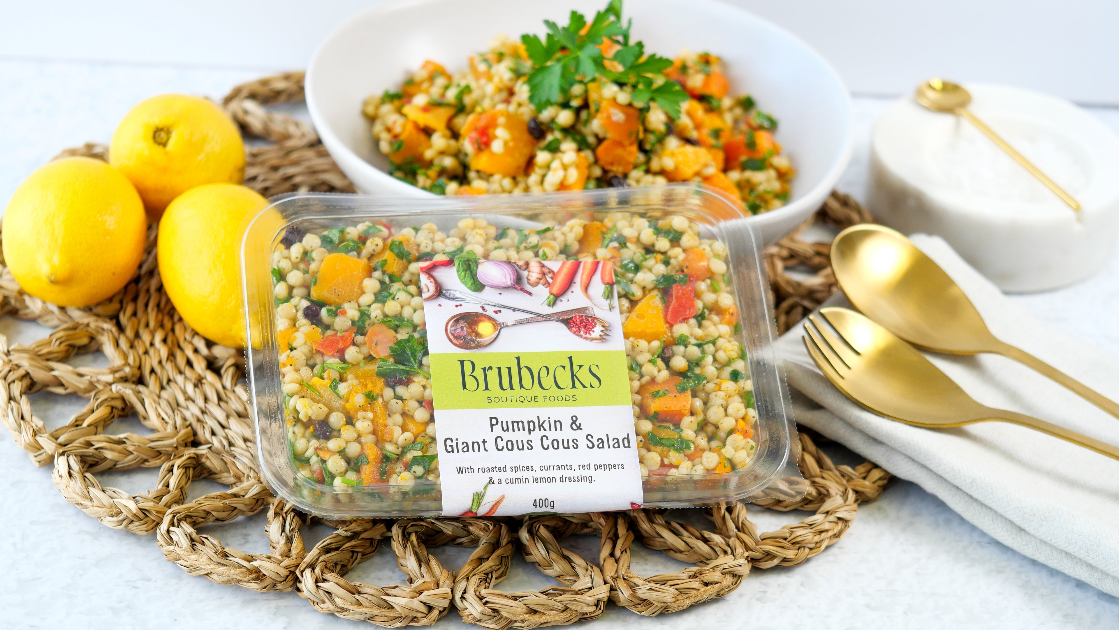 Brubecks salad packaging with a bowl of salad, lemons, and gold utensils on a textured surface.