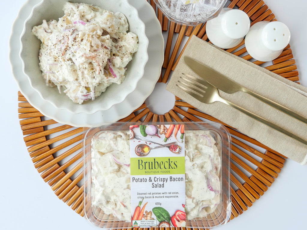 Packaged salad with a bowl of salad, cutlery, and candles on a wooden mat.