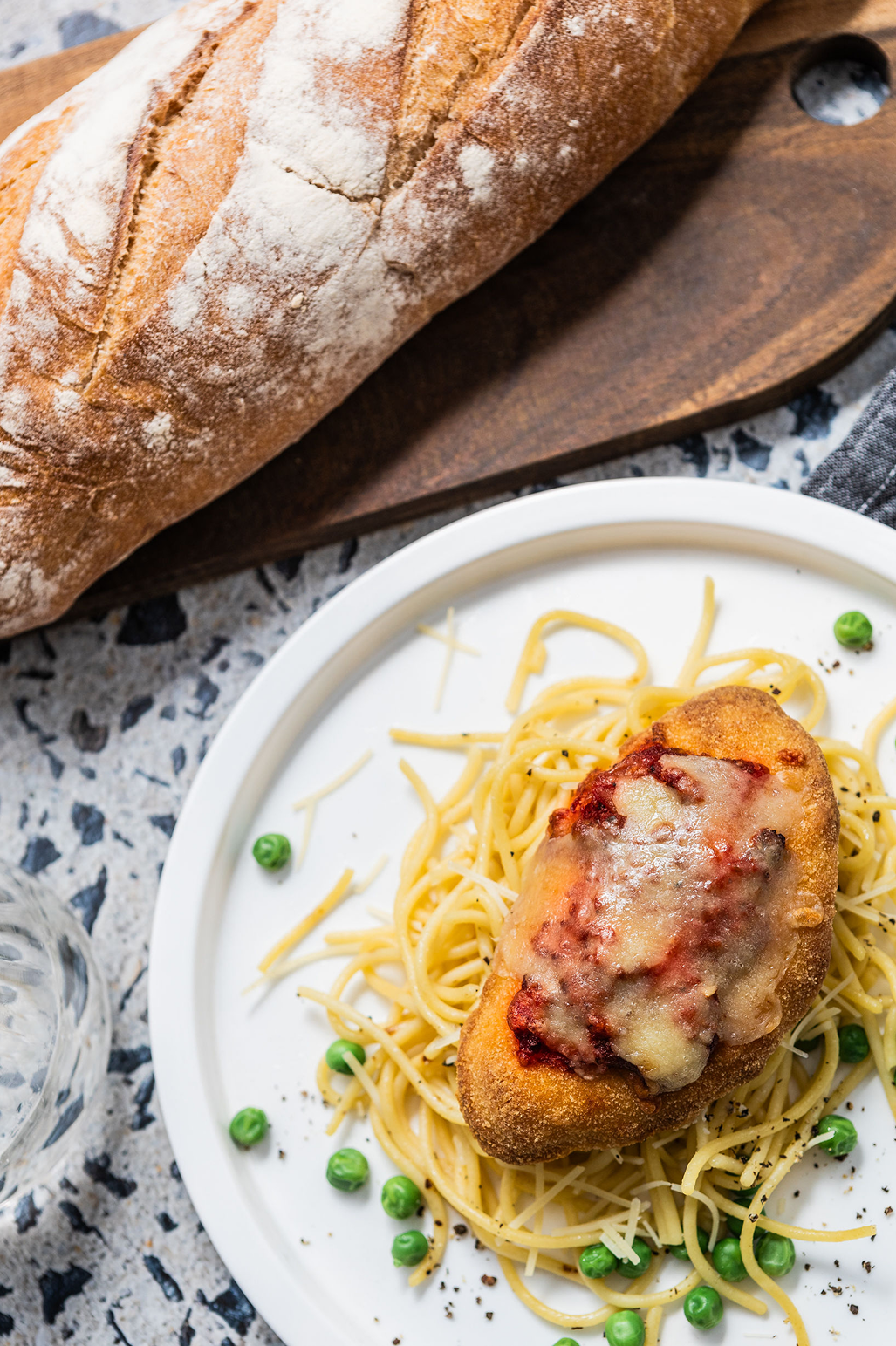 Brubecks dish of spaghetti with meatballs and peas, accompanied by a loaf of bread on a wooden board.