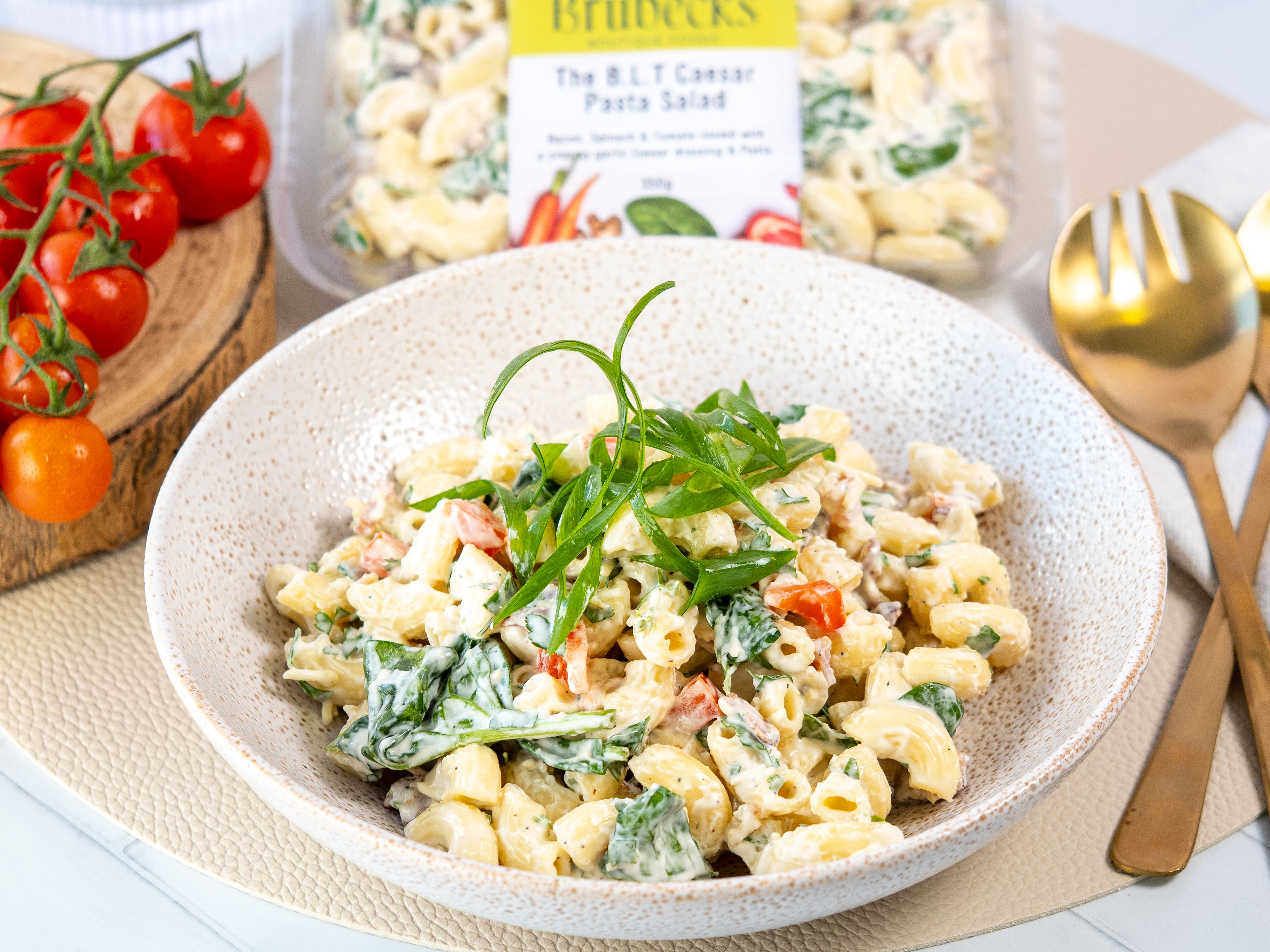 Pasta salad in a bowl with greens and tomatoes, next to a package of pasta, on a table.