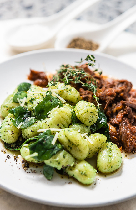 Plate of Brubecks gnocchi with pesto and spinach, served with a side of braised meat.