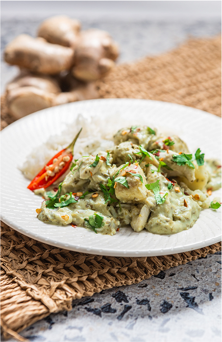Plated dish of Brubecks green curry with chicken and rice, garnished with cilantro, on a textured surface.