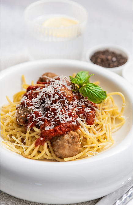 Brubecks spaghetti with meatballs on a white plate, garnished with basil and parmesan cheese.