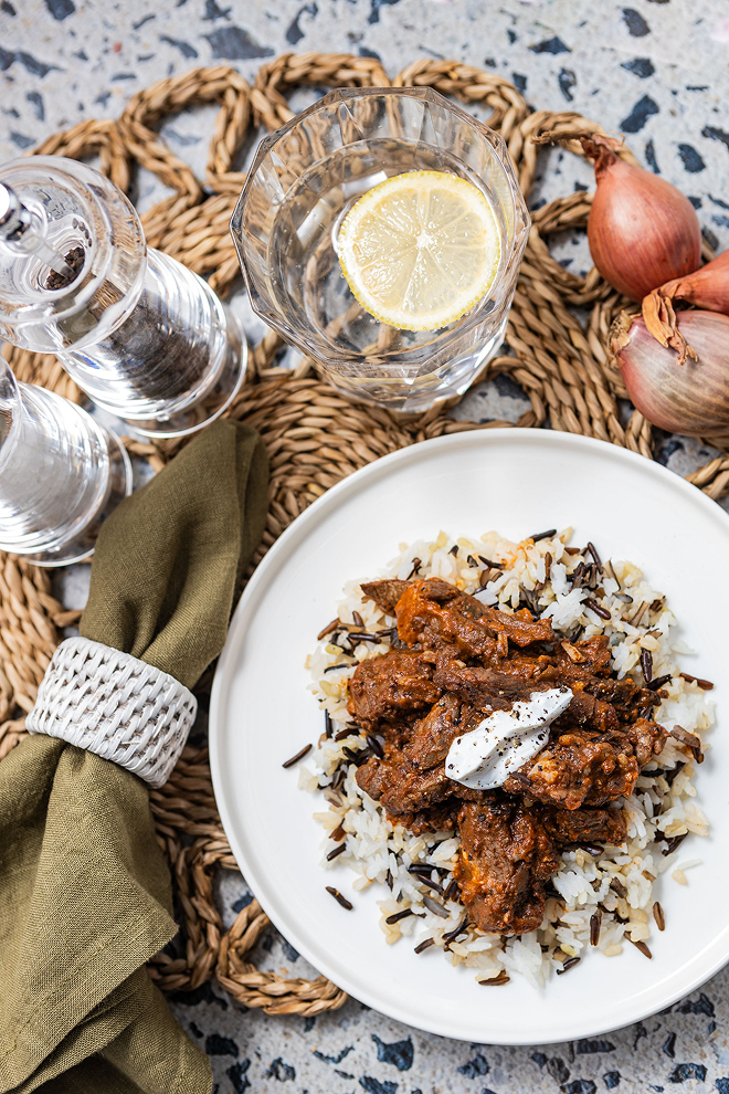 Plated dish of Brubecks beef and rice with a glass of water and lemon on a textured surface